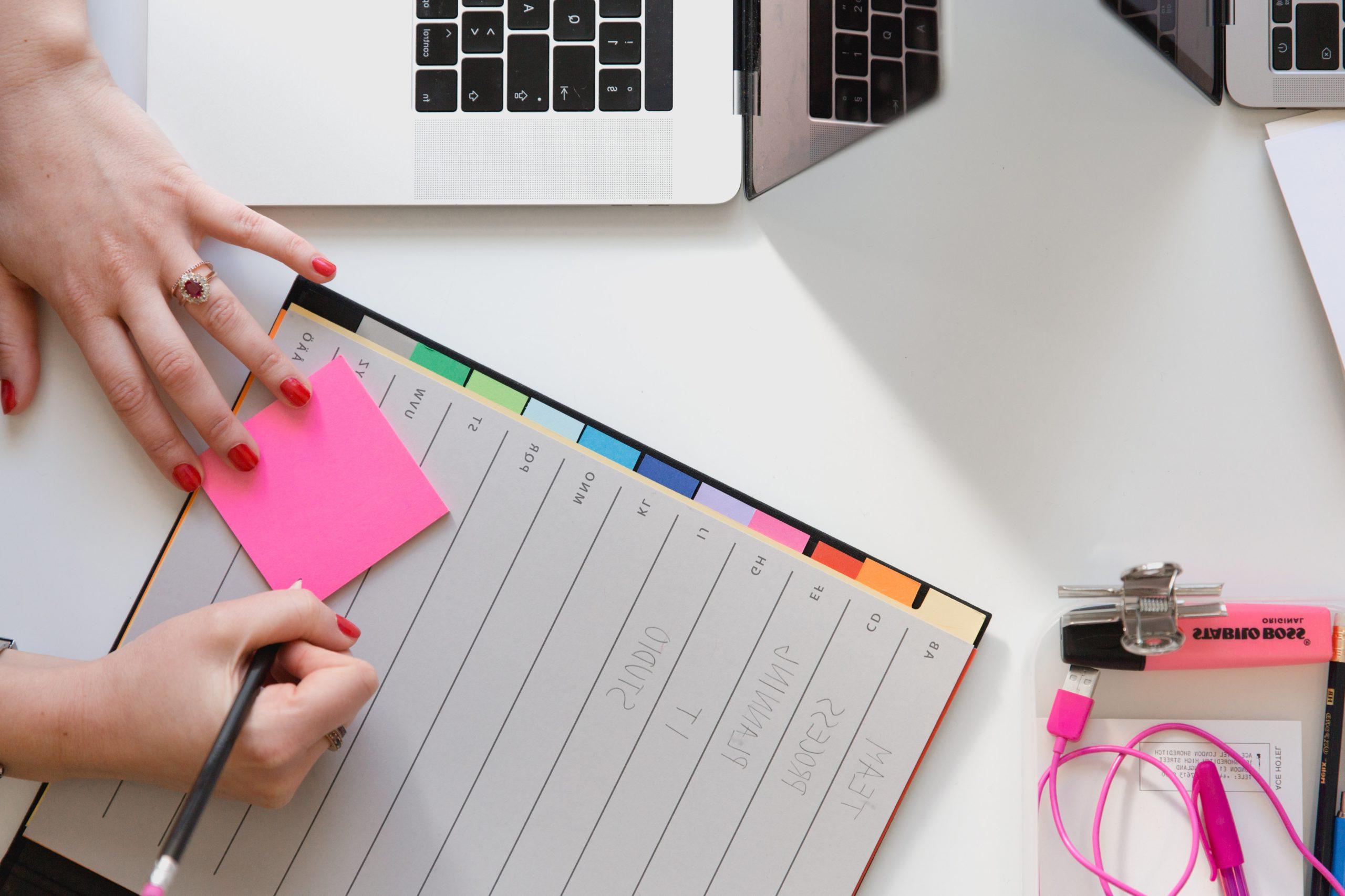 Person holding a pencil writing on pink sticky note