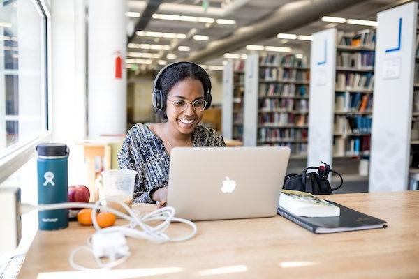 A woman with glasses and headphones works on her laptop in the Auraria library.